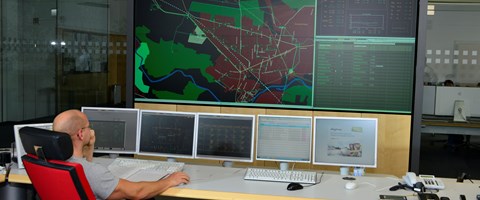 Mitarbeiter auf einem roten Stuhl vor Monitoren mit Schaltleitungen Mitarbeiter auf einem roten Stuhl vor Monitoren mit Schaltleitungen