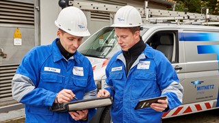 Zwei Techniker in Blaumännern betrachten Tablets vor einem Technikfahrzeug Zwei Techniker in Blaumännern betrachten Tablets vor einem Technikfahrzeug