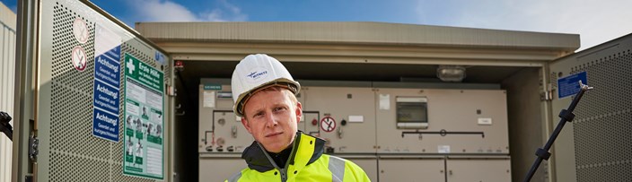 Techniker in Warnschutzjacke mit Geräten vor offener Trafostation Techniker in Warnschutzjacke mit Geräten vor offener Trafostation