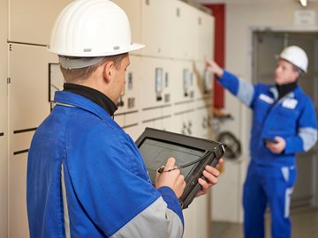 Techniker mit portablem Eingabegerät steht mit Kollegen vor einer Anlage Techniker mit portablem Eingabegerät steht mit Kollegen vor einer Anlage