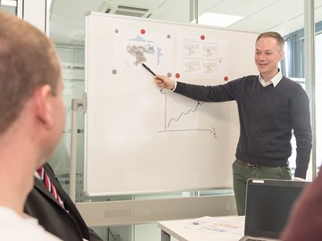 Mann deutet in einem Konferenzraum mit Kugelschreiber auf ein Präsentations-Chart Mann deutet in einem Konferenzraum mit Kugelschreiber auf ein Präsentations-Chart