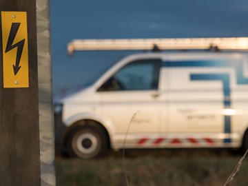 Warnschild vor gefährlicher elektrischer Spannung mit Technikfahrzeug im Hintergrund Warnschild vor gefährlicher elektrischer Spannung mit Technikfahrzeug im Hintergrund