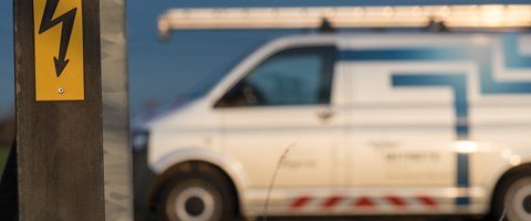 Warnschild vor gefährlicher elektrischer Spannung mit Technikfahrzeug im Hintergrund Warnschild vor gefährlicher elektrischer Spannung mit Technikfahrzeug im Hintergrund