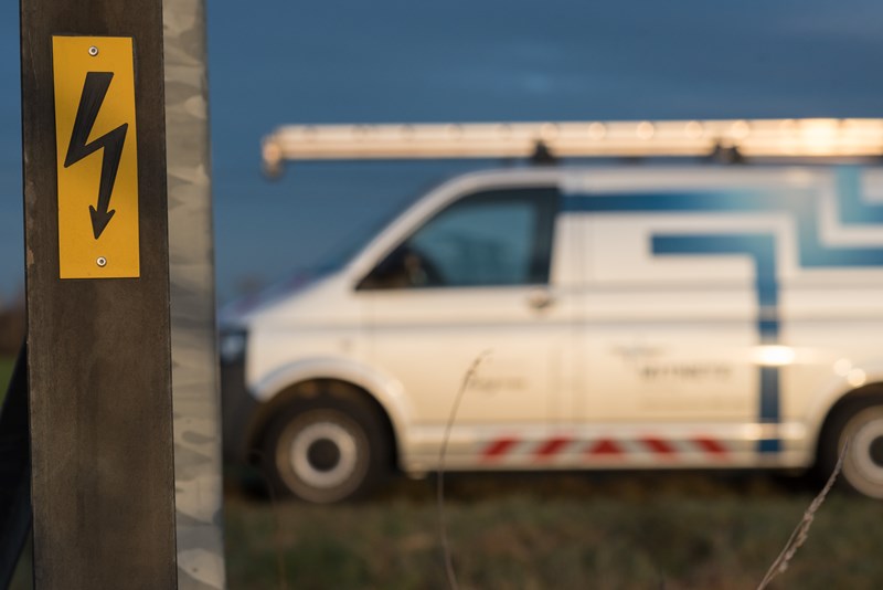 Warnschild vor gefährlicher elektrischer Spannung mit Technikfahrzeug im Hintergrund