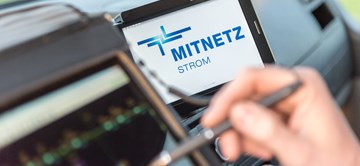 Portables Eingabegerät und Smartphone, auf dem das MITNETZ STROM-Logo zu sehen ist, im Innern eines Fahrzeugs Portables Eingabegerät und Smartphone, auf dem das MITNETZ STROM-Logo zu sehen ist, im Innern eines Fahrzeugs
