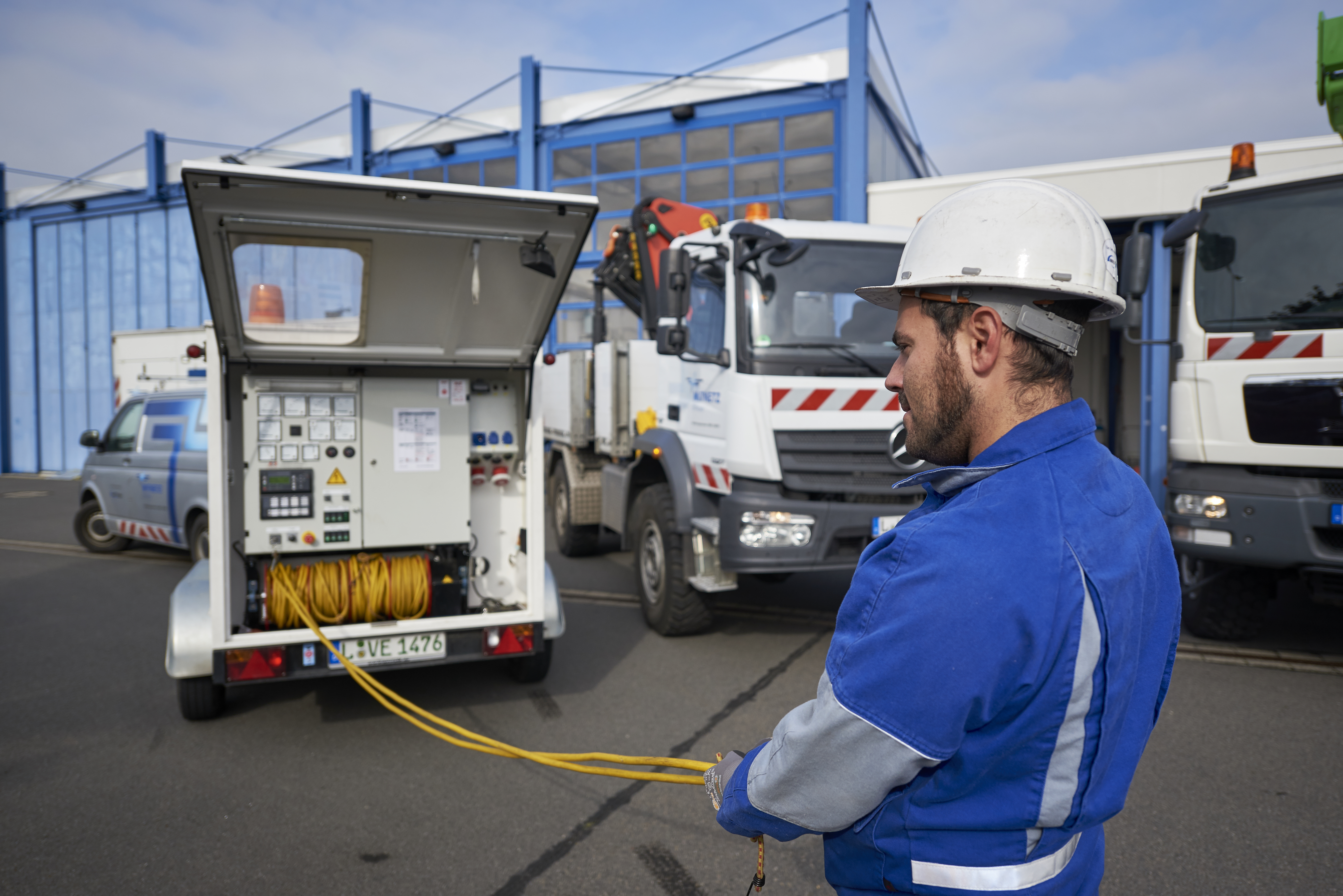 Mitarbeiter in Helm und Blaumann entrollt ein Kabel aus einem Anhänger neben zwei Lkw