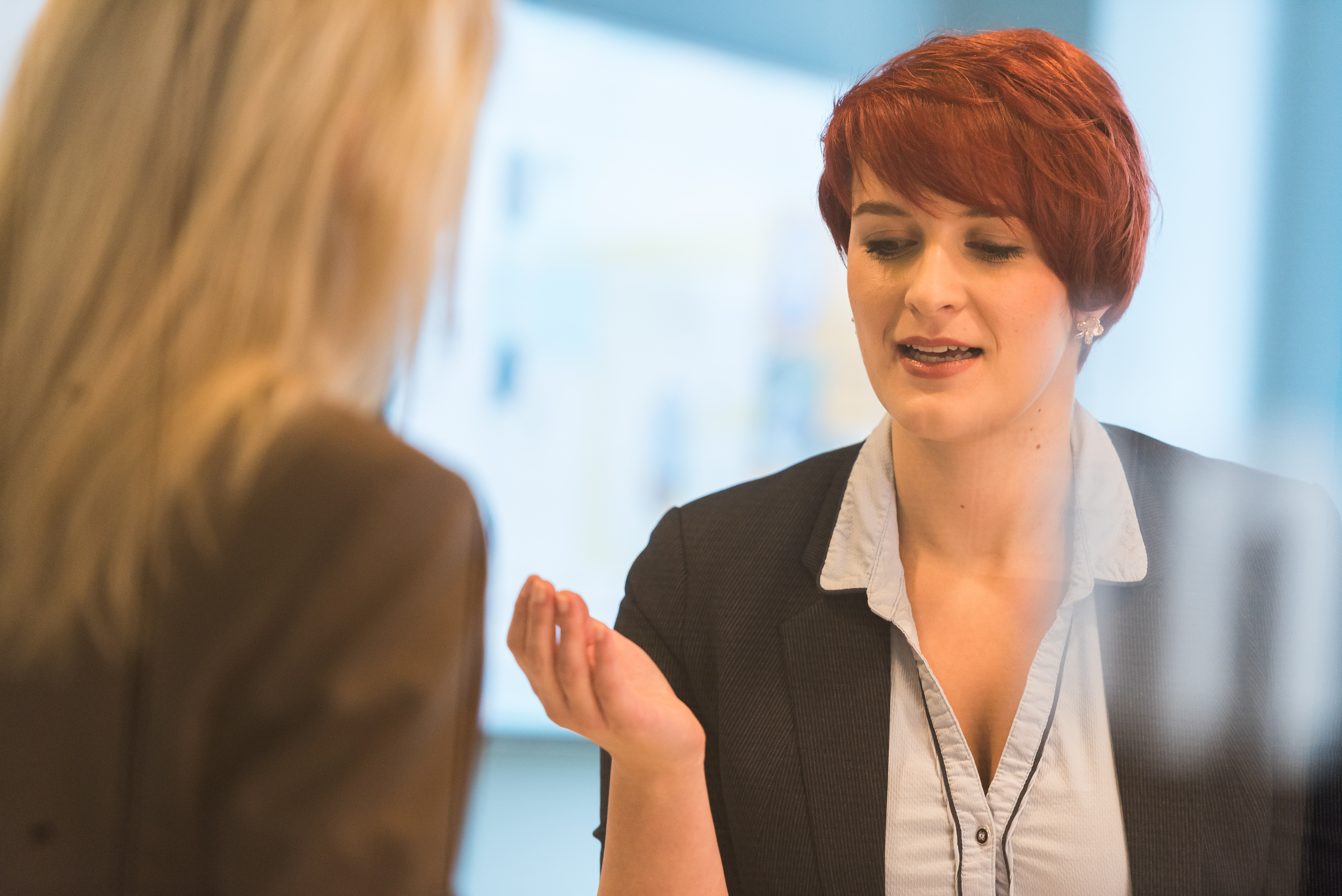 yZwei Frauen in Business-Kleidung im Gespräch, durch eine reflektierende Scheibe fotografiert