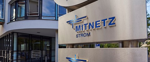 Großes MITNETZ STROM-Logo, blau auf grauem Stahl, am Eingang eines Firmengebäudes Großes MITNETZ STROM-Logo, blau auf grauem Stahl, am Eingang eines Firmengebäudes