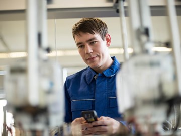 Techniker mit kleinem Messgerät in beiden Händen blickt konzentriert auf Geräte Techniker mit kleinem Messgerät in beiden Händen blickt konzentriert auf Geräte