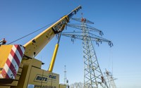 Kran vor einem Hochspannungsmast, in dem mehrere Monteure arbeiten Kran vor einem Hochspannungsmast, in dem mehrere Monteure arbeiten