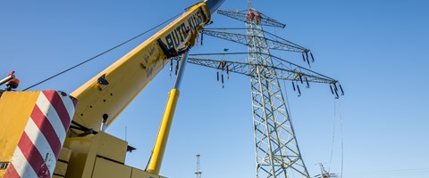 Kran vor einem Hochspannungsmast, in dem mehrere Monteure arbeiten Kran vor einem Hochspannungsmast, in dem mehrere Monteure arbeiten