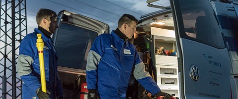 Zwei Techniker in blauen Overalls laden vor einer Abendstimmung Geräte aus einem Fahrzeug Zwei Techniker in blauen Overalls laden vor einer Abendstimmung Geräte aus einem Fahrzeug
