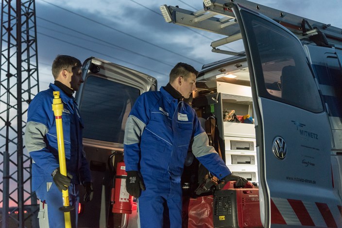 Zwei Techniker in blauen Overalls laden vor einer Abendstimmung Geräte aus einem Fahrzeug Zwei Techniker in blauen Overalls laden vor einer Abendstimmung Geräte aus einem Fahrzeug