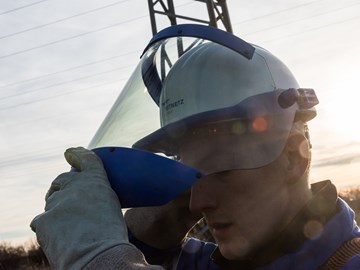 Ein Techniker unter Hochspannungsleitungen schiebt das Visier seines Helms zurück Ein Techniker unter Hochspannungsleitungen schiebt das Visier seines Helms zurück