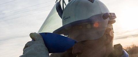 Ein Techniker unter Hochspannungsleitungen schiebt das Visier seines Helms zurück Ein Techniker unter Hochspannungsleitungen schiebt das Visier seines Helms zurück