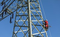Monteur im roten Overall auf einem Hochspannungsmast vor blauem Himmel Monteur im roten Overall auf einem Hochspannungsmast vor blauem Himmel