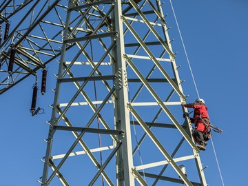 Monteur im roten Overall auf einem Hochspannungsmast vor blauem Himmel Monteur im roten Overall auf einem Hochspannungsmast vor blauem Himmel