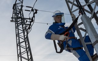 Monteur im Blaumann mit Schutzvisier am Helm sichert sich an einem Hochspannungsmast Monteur im Blaumann mit Schutzvisier am Helm sichert sich an einem Hochspannungsmast