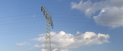 Hochspannungsmast auf einer grünen Wiese mit Windrädern unter blauem Himmel mit weißen Wolken Hochspannungsmast auf einer grünen Wiese mit Windrädern unter blauem Himmel mit weißen Wolken