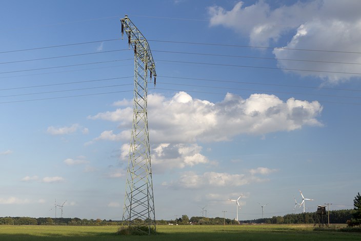 Hochspannungsmast auf einer grünen Wiese mit Windrädern unter blauem Himmel mit weißen Wolken Hochspannungsmast auf einer grünen Wiese mit Windrädern unter blauem Himmel mit weißen Wolken