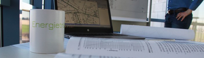 Im Vordergrund eine Tasse, ein Buch und ein Laptop auf dem die Zielnetzplanung zu sehen ist im Hintergrund eine Zielnetzplanung auf einer Pinnwand Im Vordergrund eine Tasse, ein Buch und ein Laptop auf dem die Zielnetzplanung zu sehen ist im Hintergrund eine Zielnetzplanung auf einer Pinnwand