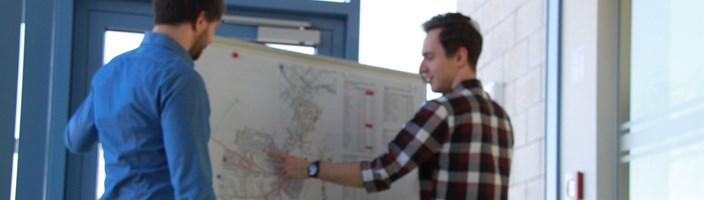 Zwei Personen stehen vor einer Pinnwand und sprechen über eine Zielnetzplanung 2 Personen stehen vor einer Pinnwand und sprechen über eine Zielnetzplanung