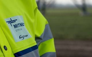 Warnschutzjacke mit MITNETZ STROM-Logo vor einem Hochspannungsmast Warnschutzjacke mit MITNETZ STROM-Logo vor einem Hochspannungsmast