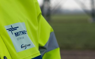 Warnschutzjacke mit MITNETZ STROM-Logo vor einem Hochspannungsmast Warnschutzjacke mit MITNETZ STROM-Logo vor einem Hochspannungsmast