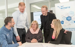 Fünf Personen, drei sitzend, zwei stehend, an einem Tisch im Konferenzraum Fünf Personen, drei sitzend, zwei stehend, an einem Tisch im Konferenzraum