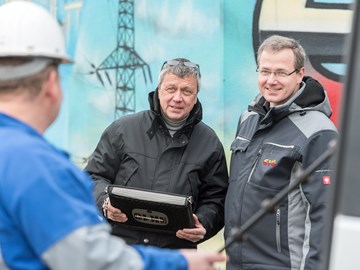 Zwei Männer in Parkern im Gespräch mit einem Arbeiter vor einem Hochspannungsmast Zwei Männer in Parkern im Gespräch mit einem Arbeiter vor einem Hochspannungsmast
