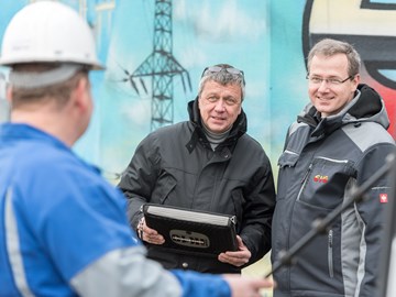 Zwei Männer in Parkern im Gespräch mit einem Arbeiter vor einem Hochspannungsmast Zwei Männer in Parkern im Gespräch mit einem Arbeiter vor einem Hochspannungsmast