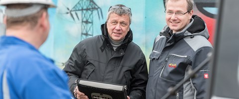 Zwei Männer in Parkern im Gespräch mit einem Arbeiter vor einem Hochspannungsmast Zwei Männer in Parkern im Gespräch mit einem Arbeiter vor einem Hochspannungsmast
