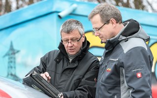 Zwei Männer in Parkern betrachten ein portables Eingabegerät Zwei Männer in Parkern betrachten ein portables Eingabegerät