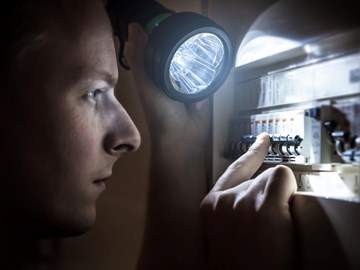 Mann mit Taschenlampe am Stromkasten Mann mit Taschenlampe am Stromkasten