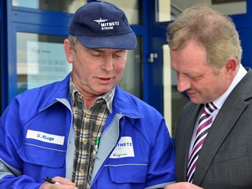 Mann im Anzug im Gespräch mit einem Mitarbeiter im Blaumann vor einem Gebäude Mann im Anzug im Gespräch mit einem Mitarbeiter im Blaumann vor einem Gebäude