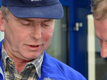 Mann im Anzug im Gespräch mit einem Mitarbeiter im Blaumann vor einem Gebäude Mann im Anzug im Gespräch mit einem Mitarbeiter im Blaumann vor einem Gebäude