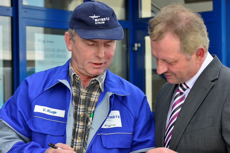 Mann im Anzug im Gespräch mit einem Mitarbeiter im Blaumann vor einem Gebäude