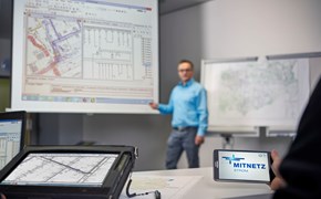 Laptop, portables Eingabegerät und Smartphone mit MITNETZ STROM-Logo - im Hintergrund hält ein Redner vor einem Plan seine Präsentation Laptop, portables Eingabegerät und Smartphone mit MITNETZ STROM-Logo - im Hintergrund hält ein Redner vor einem Plan seine Präsentation