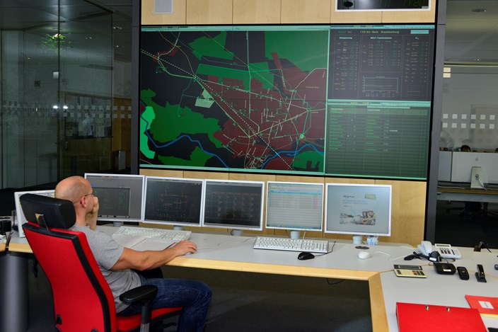 Mitarbeiter auf einem roten Stuhl vor Monitoren mit Schaltleitungen Mitarbeiter auf einem roten Stuhl vor Monitoren mit Schaltleitungen