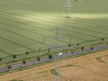 Straße zwischen Feldern über die eine Hochspannungsleitung führt - Luftaufnahme Straße zwischen Feldern über die eine Hochspannungsleitung führt - Luftaufnahme