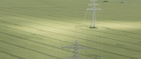 Straße zwischen Feldern über die eine Hochspannungsleitung führt - Luftaufnahme Straße zwischen Feldern über die eine Hochspannungsleitung führt - Luftaufnahme