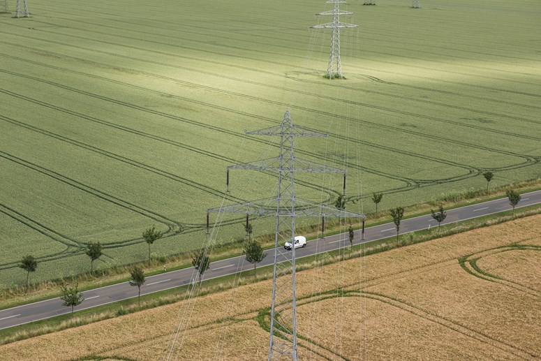 Straße zwischen Feldern über die eine Hochspannungsleitung führt - Luftaufnahme Straße zwischen Feldern über die eine Hochspannungsleitung führt - Luftaufnahme