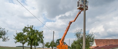 Zwei Arbeiter mit gelben Helmen in der Kanzel eines Krans, an der Spitze eines Strommasts Zwei Arbeiter mit gelben Helmen in der Kanzel eines Krans, an der Spitze eines Strommasts