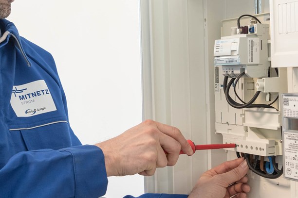 Mitarbeiter mit rotem Schraubenzieher arbeitet an einem Stromzähler Mitarbeiter mit rotem Schraubenzieher arbeitet an einem Stromzähler