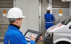 Zwei Techniker mit weißen Helmen und portablem Eingabegerät vor einer Anlage Zwei Techniker mit weißen Helmen und portablem Eingabegerät vor einer Anlage