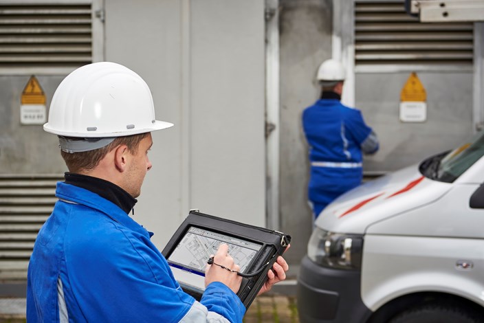 Zwei Techniker mit weißen Helmen und portablem Eingabegerät vor einer Anlage Zwei Techniker mit weißen Helmen und portablem Eingabegerät vor einer Anlage