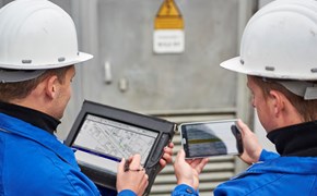 Zwei Techniker betrachten Pläne und Daten auf einem portablen Eingabegerät und einem Tablet nebeneinander Zwei Techniker betrachten Pläne und Daten auf einem portablen Eingabegerät und einem Tablet nebeneinander