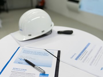 Auf einem Tisch liegen Unterlagen mit einem Kugelschreiber und ein weißer Helm Auf einem Tisch liegen Unterlagen mit einem Kugelschreiber und ein weißer Helm