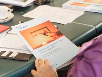 Unterlagen und Terminkalender auf einem Tisch - Hände halten eine Broschüre zum Thema Krisenmanagement Unterlagen und Terminkalender auf einem Tisch - Hände halten eine Broschüre zum Thema Krisenmanagement