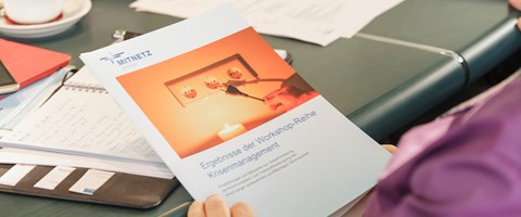 Unterlagen und Terminkalender auf einem Tisch - Hände halten eine Broschüre zum Thema Krisenmanagement Unterlagen und Terminkalender auf einem Tisch - Hände halten eine Broschüre zum Thema Krisenmanagement
